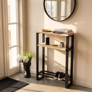 May include: A tall, narrow console table featuring a black metal frame and two light-coloured wooden shelves with natural live edges. The bottom section includes a slatted metal rack for storage, providing a sturdy structure for entryways.