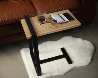 May include: A black metal side table with a wooden top. The table has a single shelf and a T-shaped base. There is a glass of liquid, a pair of glasses, a notebook, and a pen on the table.