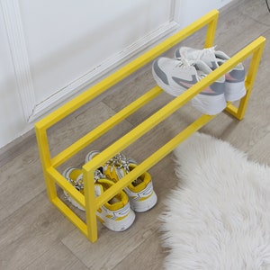 May include: A yellow metal shoe rack with two shelves. The rack is holding four pairs of shoes, two on each shelf.