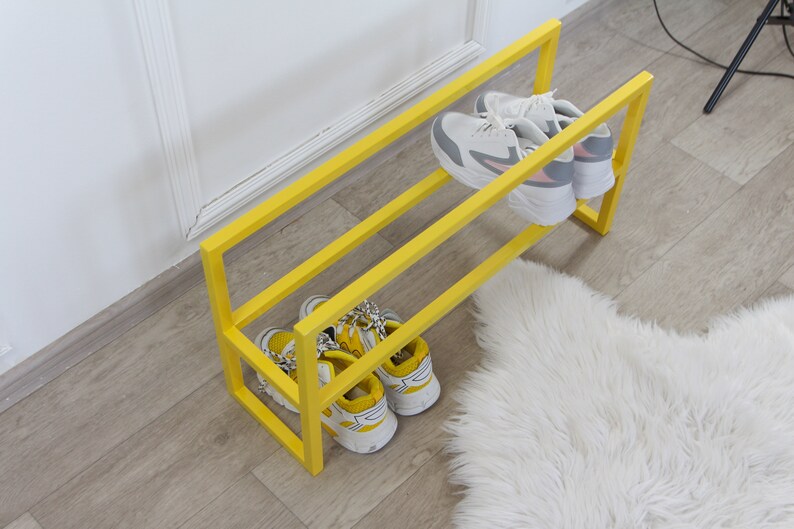 May include: A yellow metal shoe rack with two shelves. The rack is holding four pairs of shoes, two on each shelf.