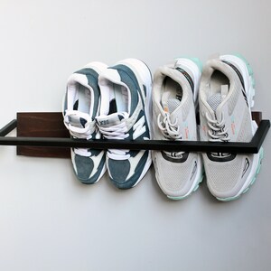 May include: A black metal shoe rack with a wooden shelf, holding four pairs of sneakers. Two pairs are blue and white, and two pairs are gray and white.