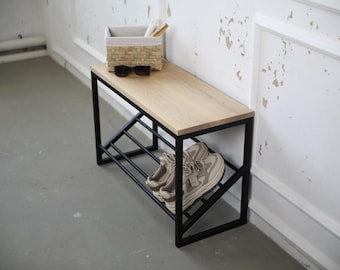 May include: A contemporary shoe bench featuring a light wood top and a black metal frame. The bench includes a lower shelf for shoe storage, with a woven basket and sunglasses on top. A pair of trainers is on the lower shelf.