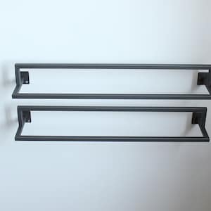 May include: Two black metal towel bars mounted on a white wall. The bars are parallel to each other and are spaced evenly apart.