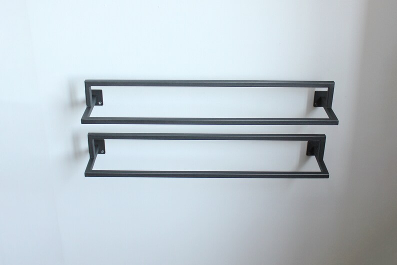 May include: Two black metal towel bars mounted on a white wall. The bars are parallel to each other and are spaced evenly apart.