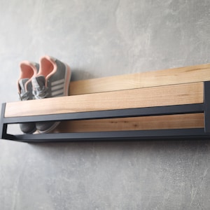 May include: A black metal shoe rack with a wooden shelf. The rack has two shelves and is mounted to a wall. Two pairs of pink and gray sneakers are on the top shelf.