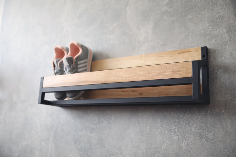 May include: A black metal shoe rack with a wooden shelf. The rack has two shelves and is mounted to a wall. Two pairs of pink and gray sneakers are on the top shelf.