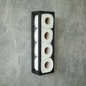 Può includere: Un portarotolo di carta igienica rettangolare nero montato su un muro grigio. Il supporto contiene quattro rotoli di carta igienica bianca. Il design è minimalista e moderno, adatto per un bagno.