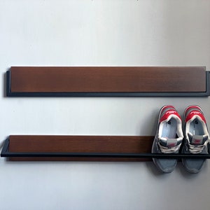 May include: Two-tiered wooden shoe rack with black metal frame. The top shelf is empty and the bottom shelf has two pairs of gray and red sneakers.