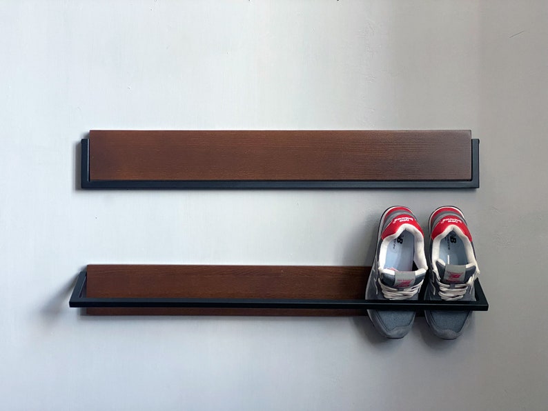 May include: Two-tiered wooden shoe rack with black metal frame. The top shelf is empty and the bottom shelf has two pairs of gray and red sneakers.
