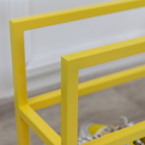 May include: A yellow metal shoe rack with two shelves. The rack is made of square metal tubing and has a simple, modern design.