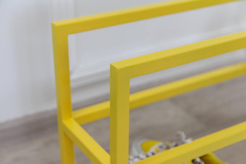 May include: A yellow metal shoe rack with two shelves. The rack is made of square metal tubing and has a simple, modern design.
