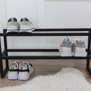 May include: Black metal shoe rack with two shelves. The top shelf has two pairs of white sneakers with blue accents. The bottom shelf has two pairs of white sneakers with pink and green accents.