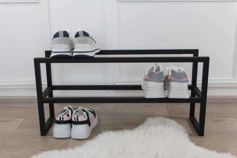 May include: Black metal shoe rack with two shelves. The top shelf has two pairs of white sneakers with blue accents. The bottom shelf has two pairs of white sneakers with pink and green accents.