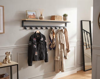 May include: A wall-mounted coat rack featuring a light wood shelf supported by a black metal frame with eight hooks. The rack holds a black denim jacket with patches, a patterned scarf, and a beige trench coat, providing organized storage.