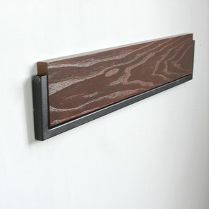 May include: A wooden shelf with a black metal frame mounted on a white wall. The shelf has a dark wood grain pattern.