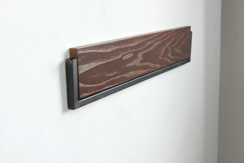 May include: A wooden shelf with a black metal frame mounted on a white wall. The shelf has a dark wood grain pattern.