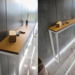 May include: A modern console table with a light oak top and white metal frame. The table has a rectangular shape and is decorated with a wooden box, keys, and a small bottle. The table is 152 cm long.