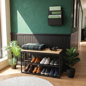 Può includere: Una scarpiera in metallo nero con due ripiani e una superficie superiore in legno chiaro. Il mobile contiene diverse paia di scarpe, tra cui sneakers, mocassini e stivaletti. Una coperta a quadri verdi e neri è ripiegata sul piano in legno.