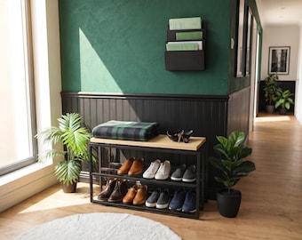 May include: A black metal shoe rack with two shelves and a light wood top surface. The rack holds various pairs of shoes, including trainers, loafers, and boots. A folded green and black plaid blanket rests on the top wooden surface of the rack.