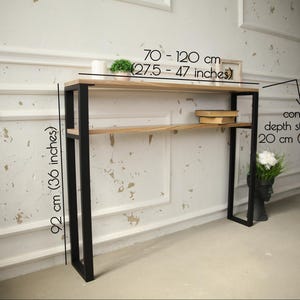 May include: A modern console table with a light wood top and a black metal frame. The table is 36 inches tall, with a top that is 27.5 to 47 inches wide and 8 inches deep. The table has two shelves.