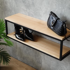 May include: A modern, two-tiered shelf with a black metal frame and light wood shelves. Black high-heeled shoes and a black handbag with a textured finish are displayed on the shelf. A potted green plant is in the foreground.