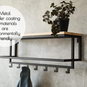 Puede incluir: Estante de pared de metal negro con una parte superior de madera y ganchos. El estante está montado en una pared gris. El texto "Metal powder coating all materials are environmentally friendly" está escrito en un círculo blanco en la esquina superior izquierda de la imagen.
