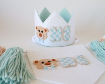 May include: A white felt crown with a blue and white checkered "ONE" and a brown bear applique. A white felt banner with a blue and white checkered "ONE" and a brown bear applique. Two tassels, one light blue and one light brown.