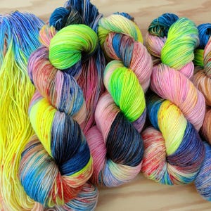 Könnte beinhalten: Nahaufnahme von bunten Garnknäueln. Das Garn ist eine Mischung aus leuchtenden Farben, darunter Gelb, Blau, Rosa und Grün. Das Garn ist auf ansprechende Weise angeordnet, wobei sich die Knäuel überlappen. Das Garn scheint weich und flauschig zu sein.
