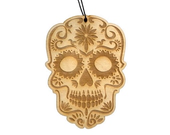 May include: A wooden ornament shaped like a sugar skull with intricate floral designs. The skull is carved with details like eyes, a nose, and a mouth.