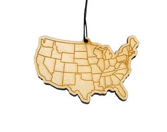 May include: A wooden ornament shaped like the United States of America with state borders outlined. The ornament is light brown and has a black string for hanging.