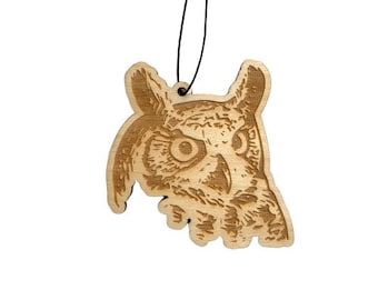 May include: A wooden owl car air freshener with a brown wood finish and a detailed engraving of an owl's face. The owl is looking to the right and has large, round eyes.