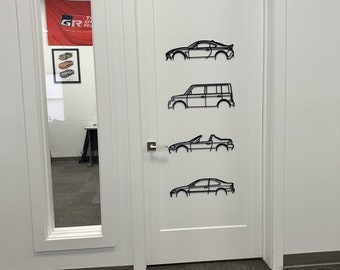 May include: A white door with four black metal car silhouettes attached to it. The silhouettes are of a sports car, a minivan, a convertible, and a sedan.