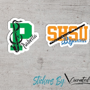 May include: Two vinyl stickers with a musical theme. The first sticker is green with a black saxophone and the letter "P" and the name "Isabella". The second sticker is orange with a black flute and the letters "SHSU" and the name "Bryanna".