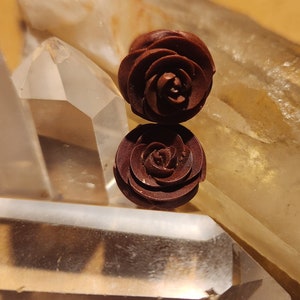 May include: Two brown wooden rose-shaped earrings. The earrings are carved with intricate details and have a natural wood finish.