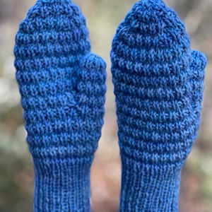 May include: A pair of blue knitted mittens with a textured pattern. The mittens are made of a soft, warm yarn and have a ribbed cuff.