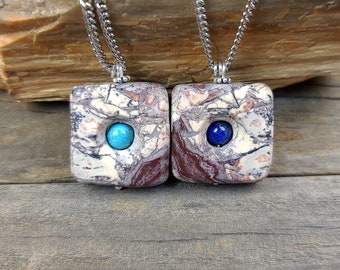 May include: Two square pendants on silver chains. The pendants are made of marbled stone with a blue gemstone set in the center of each. One pendant has a turquoise gemstone and the other has a lapis lazuli gemstone.