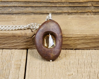 May include: A brown stone pendant with a clear crystal inside. The pendant is on a silver chain.