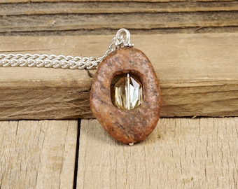 May include: A brown stone pendant with a clear crystal in the center, hanging from a silver chain.