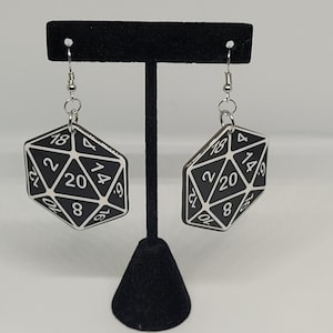 May include: A pair of black and white d20 dice earrings. The dice are made of wood and have a silver metal hook.