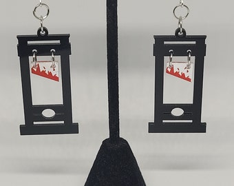 Puede incluir: Un par de pendientes de guillotina negros con detalles rojos y blancos. Los pendientes cuelgan de ganchos plateados.