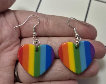 Könnte beinhalten: Ein Paar herzförmige Ohrringe mit Regenbogen-Design. Jeder Ohrring hat einen silbernen Haken und ein gestreiftes Muster in Rot, Orange, Gelb, Grün, Blau und Lila. Ein farbenfrohes Accessoire.
