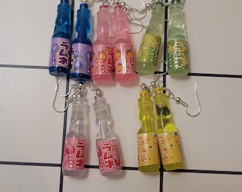Puede incluir: Un conjunto de seis pares de pendientes colgantes con botellas de plástico en miniatura con texto japonés y líquido de colores. Las botellas son en tonos de azul, rosa, verde y amarillo.