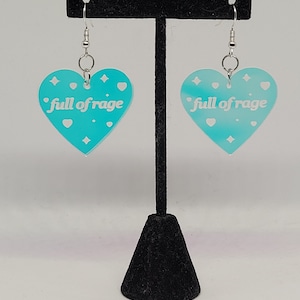 May include: A pair of heart-shaped earrings in a vibrant turquoise hue, each featuring the phrase "full of rage" in white. The earrings have a gradient effect and are adorned with small star and heart shapes. They hang from silver-colored hooks.