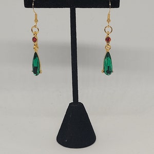 May include: A pair of gold dangle earrings with green teardrop-shaped crystals and red accent beads.