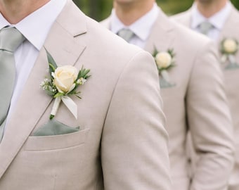 May include: Three men in light tan suits with white shirts and light green ties. Each suit has a cream-colored rose boutonniere and a matching pocket square. The men are smiling, suggesting a celebratory event.