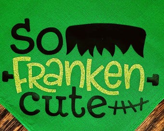 May include: Green pet bandana with the phrase "So Franken Cute" in black and glittery lime green lettering. The design includes a black Frankenstein-like hair silhouette and stitches, perfect for Halloween.