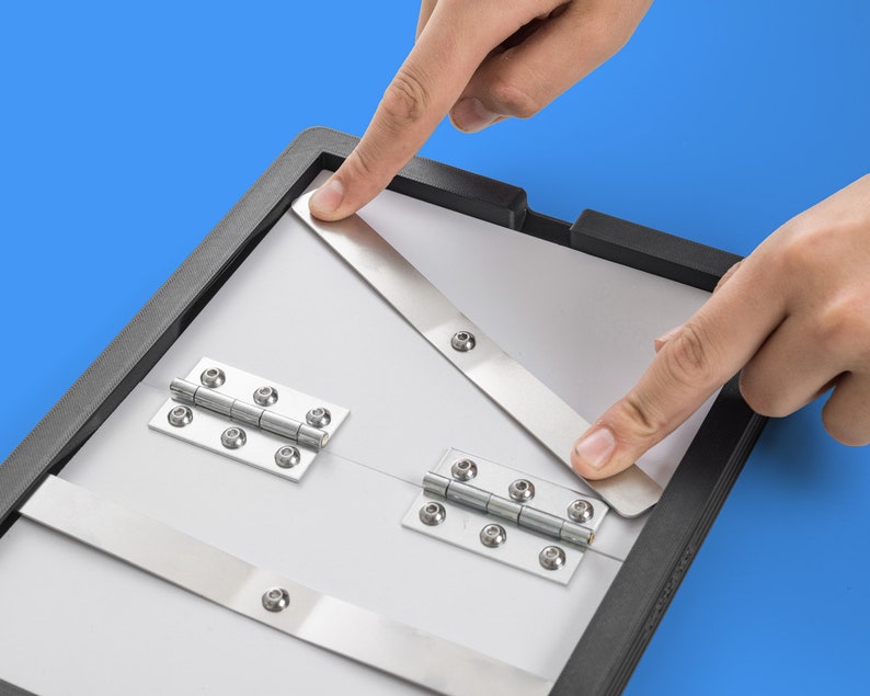May include: A black frame with two white panels connected by silver hinges. The panels are held together by two silver metal bars. The frame is being held by two hands.
