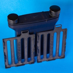 Może przedstawiać: Czarny plastikowy zbiornik do wywoływania filmu z dwoma wyjmowanymi szpulami do wywoływania filmu. Zbiornik ma dwie czarne nakrętki na górze. Szpule mają nadrukowany tekst "Stainless Steel".