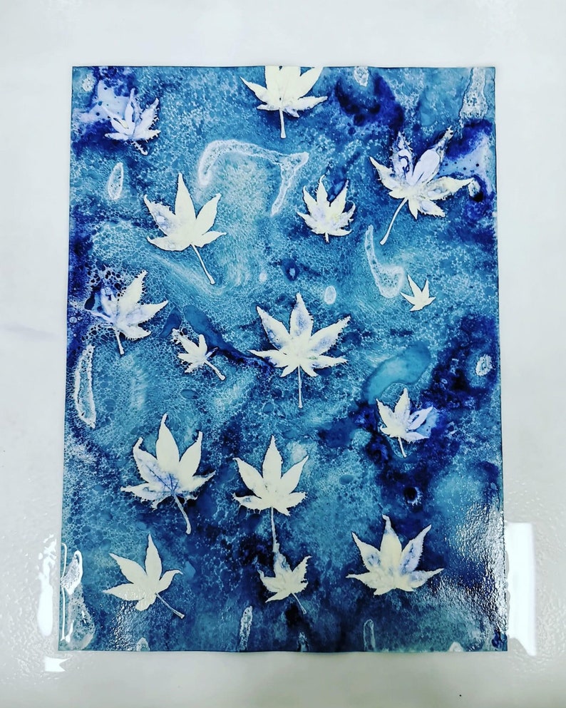 Op de afbeelding: Een abstracte kunstprint met een patroon van witte bladeren op een blauwe achtergrond.