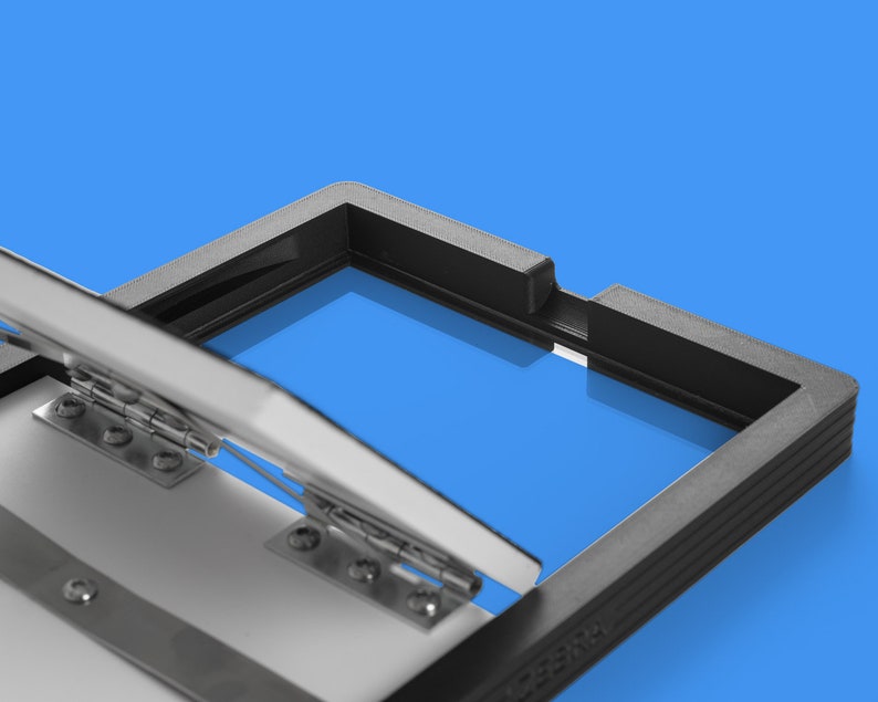 May include: A black plastic frame with a hinged lid. The lid is open and the frame is reflecting the blue background.